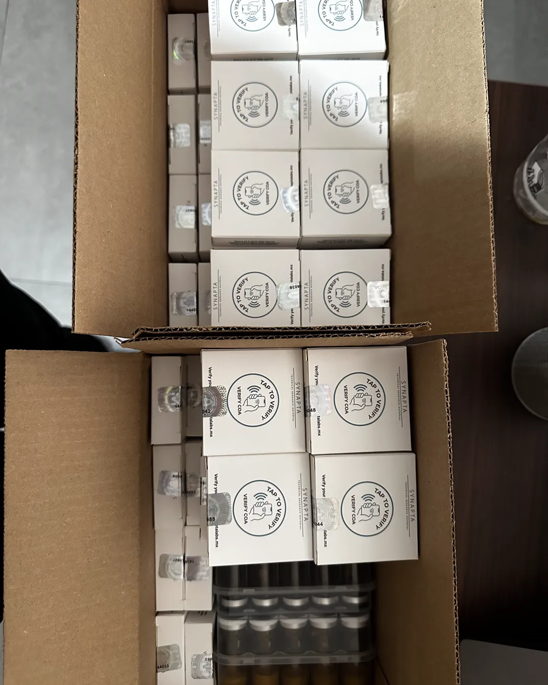 Cajas Synapta Labs listas para envío, cada una con sello holográfico y sticker NFC